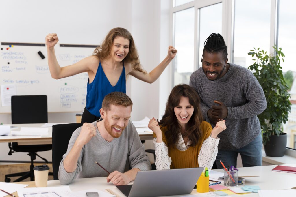 Four employees standing around a computer celebrating a win